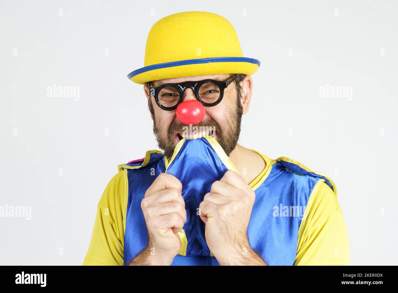 Holiday concept. A clown in a bright blue and yellow suit bites his tie from fright Stock Photo