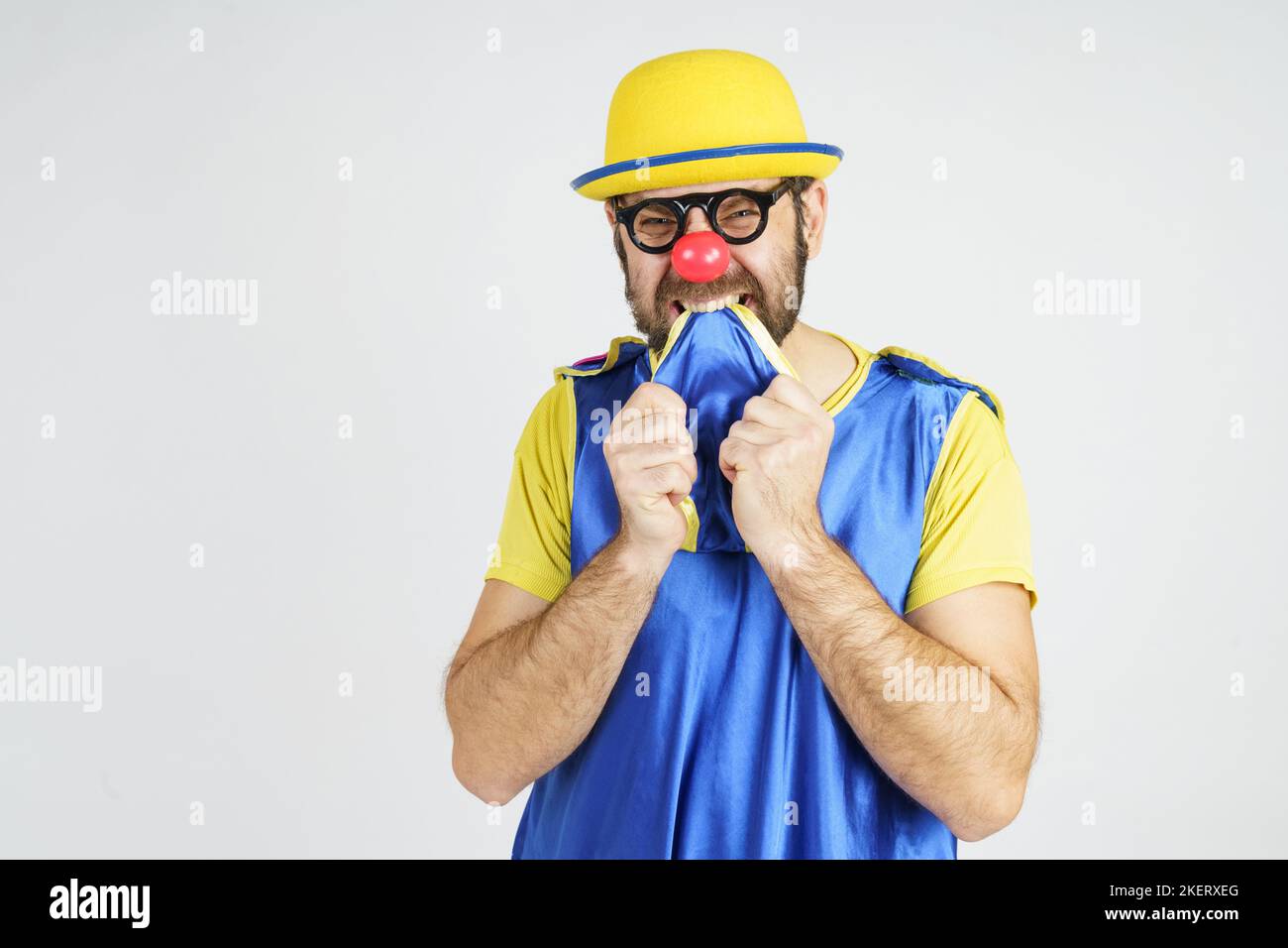 Holiday concept. A clown in a bright blue and yellow suit bites his tie from fright Stock Photo