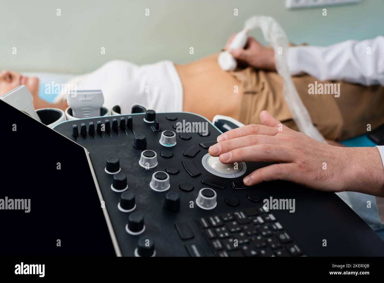 partial view of doctor operating ultrasound machine while doing abdominal examination of blurred woman,stock image Stock Photo