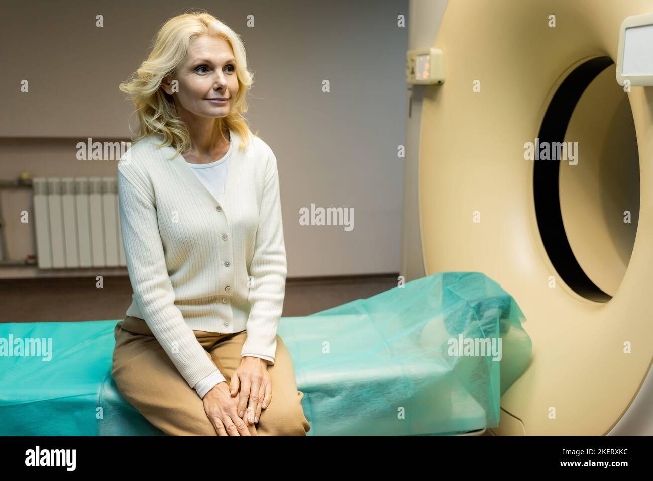 smiling middle aged woman sitting near computed tomography scanner in ...