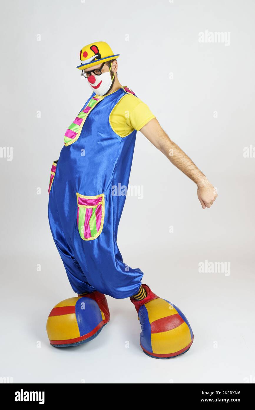 Holiday concept. A clown in a bright blue and yellow suit, glasses and ...