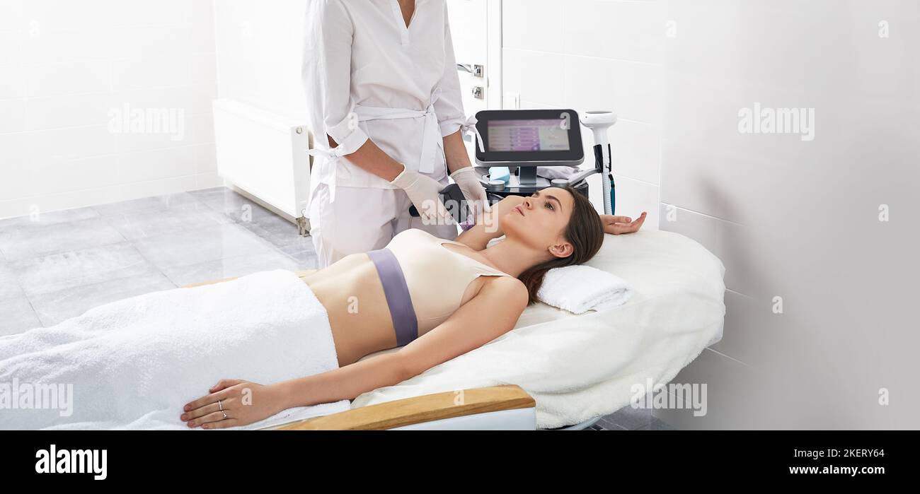 Woman having RF lifting procedure for skin tightening of her hands and body with beautician at cosmetology center. RF lifting Stock Photo