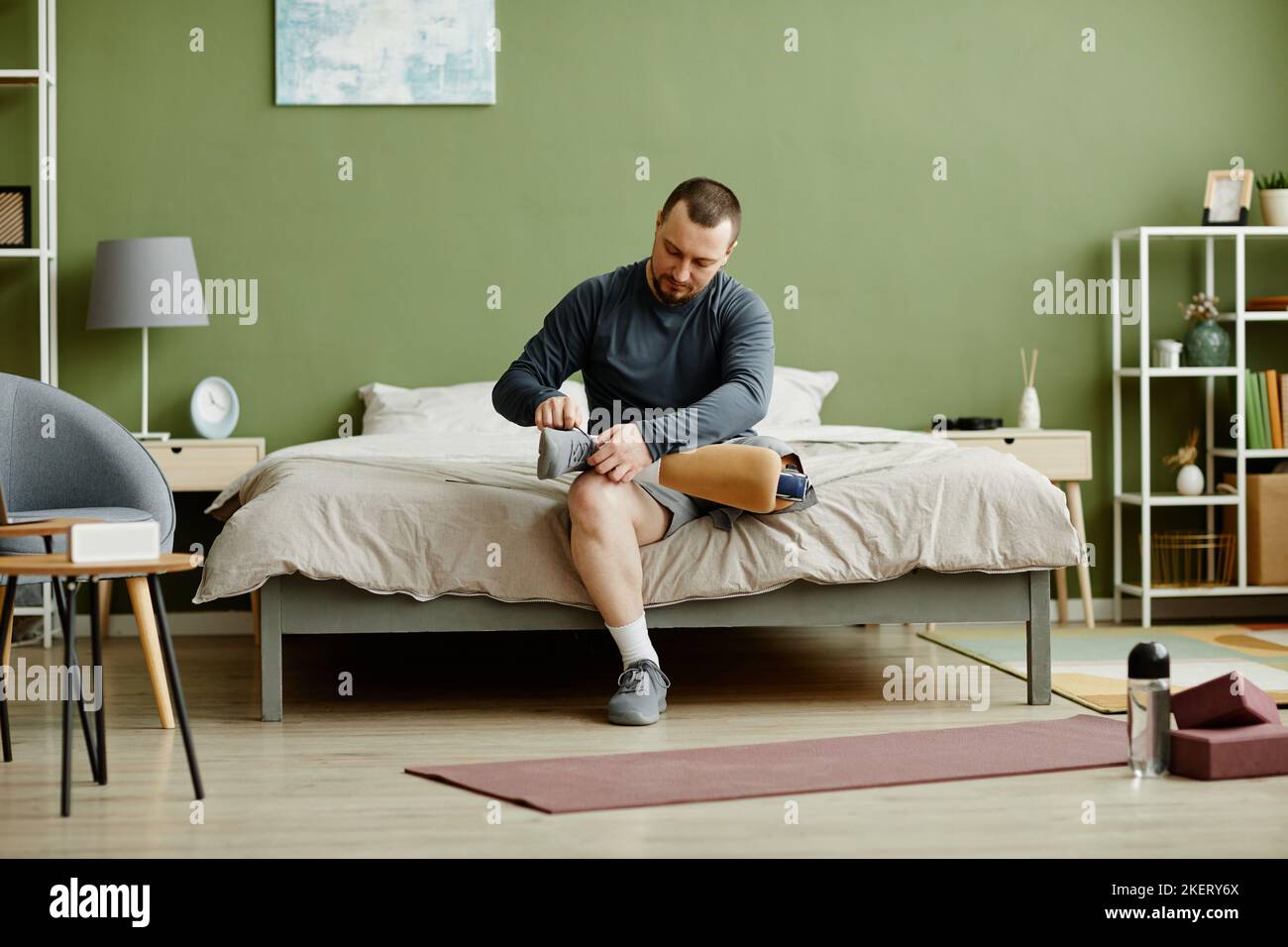 Full length portrait of adult man fixing prosthetic leg and getting ready to work out at home, copy space Stock Photo