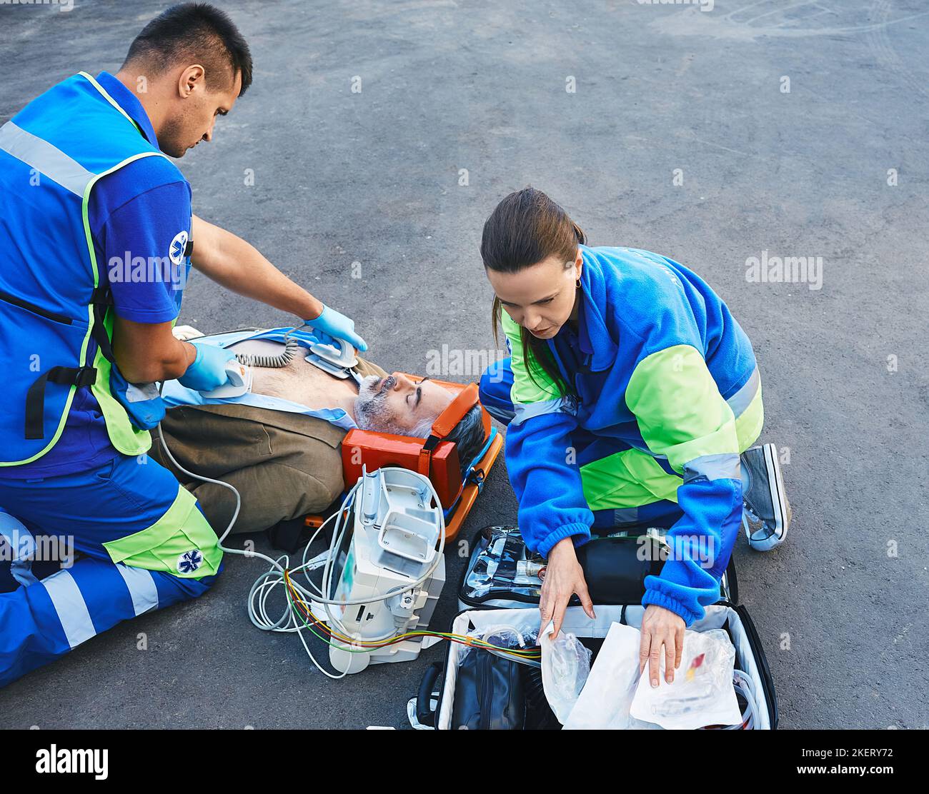 Paramedics performing CPR with mobile defibrillator for victim man lying in stretcher outside