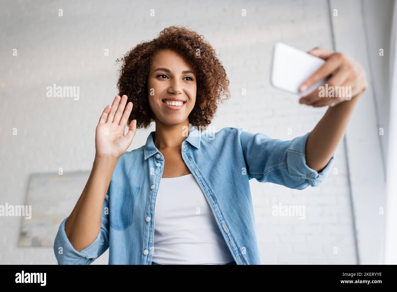 happy african american woman with curly hair waving hand during video ...