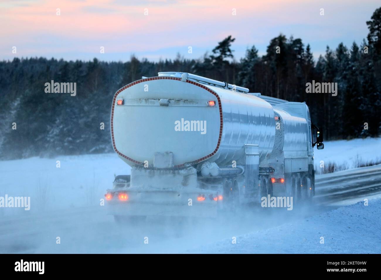 Rear view of snowy fuel tanker truck trucking along highway in winter