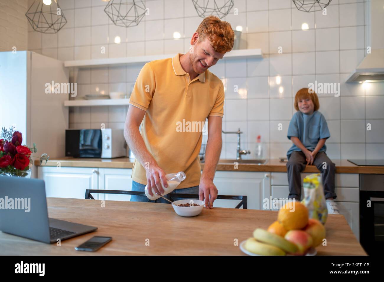 Ginger man with a bottle of milk in hands getting ready the breakfast for his son Stock Photo