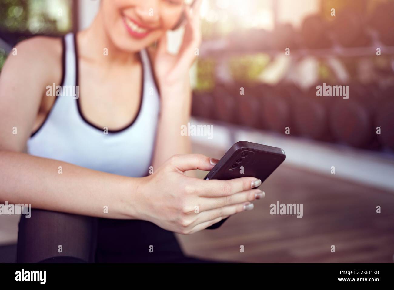 Young woman sitting on yoga mat after exercising, relaxing with smartphone and listening to music. Stock Photo