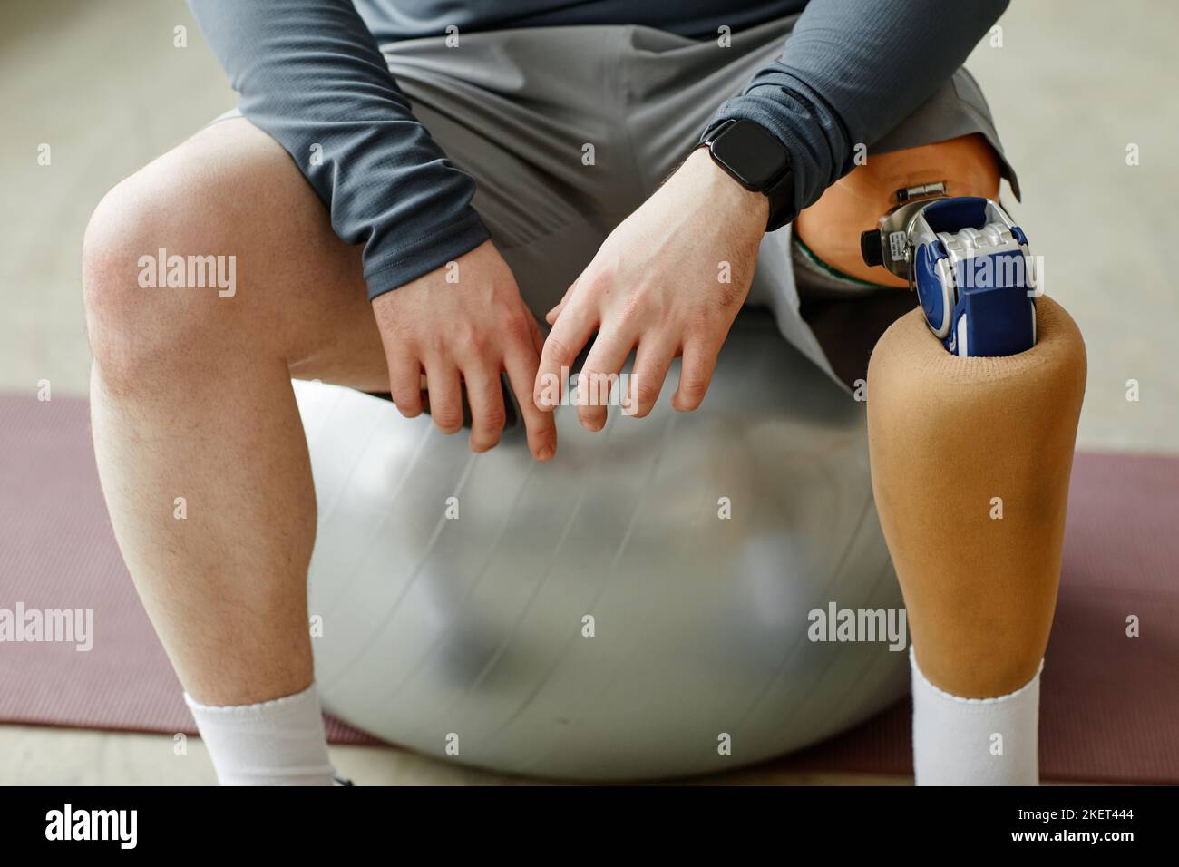 Close up of man with prosthetic leg sitting on fitness ball during home workout Stock Photo
