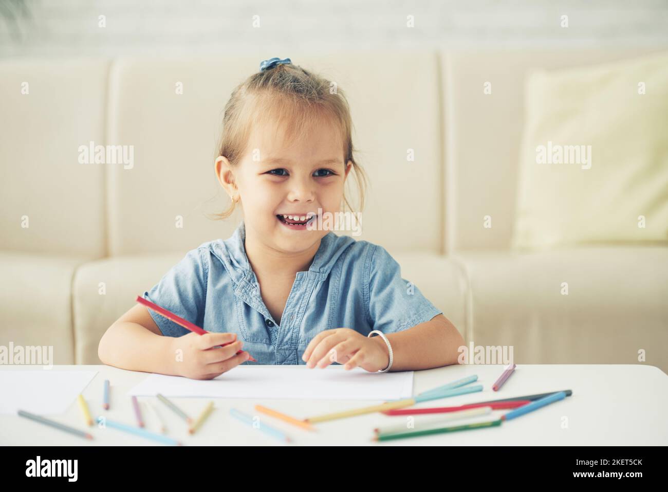 Portrait of laughing little girl drawing at table in living room Stock ...