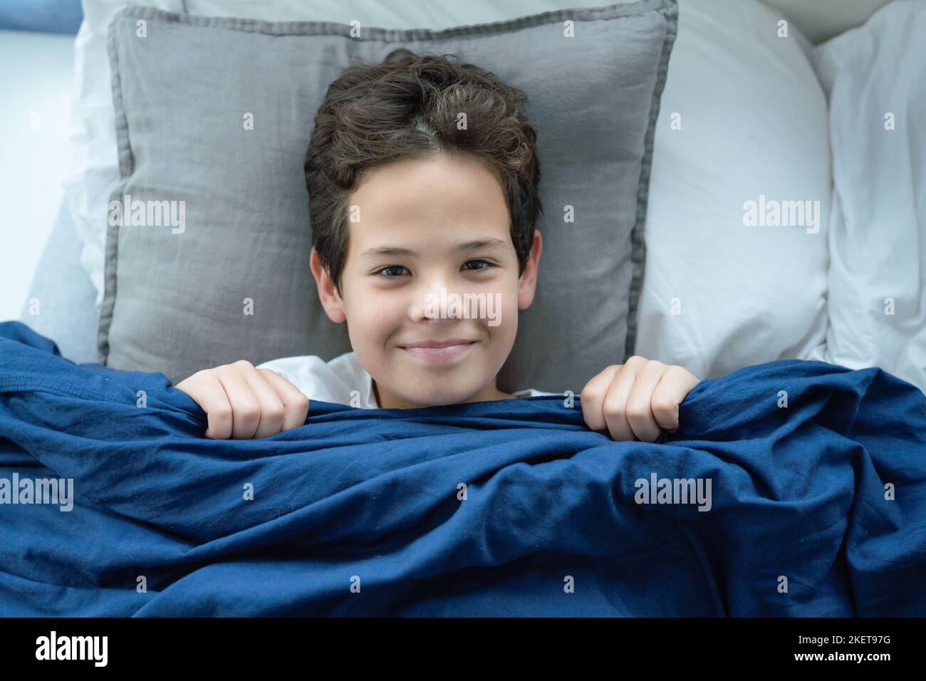 Smiling preteen boy child lying in bed and covering his tricky playful