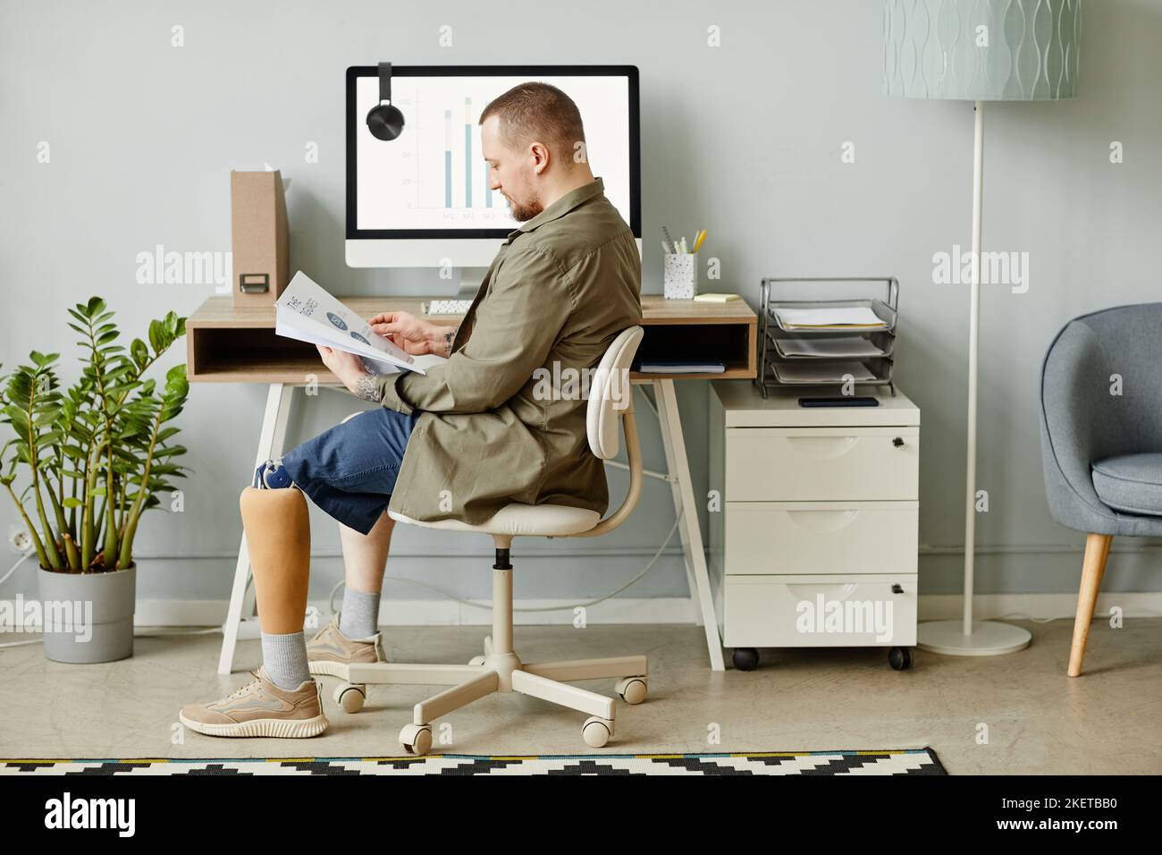 Minimal full length portrait of man with prosthetic leg working at home office and reading documents, copy space Stock Photo