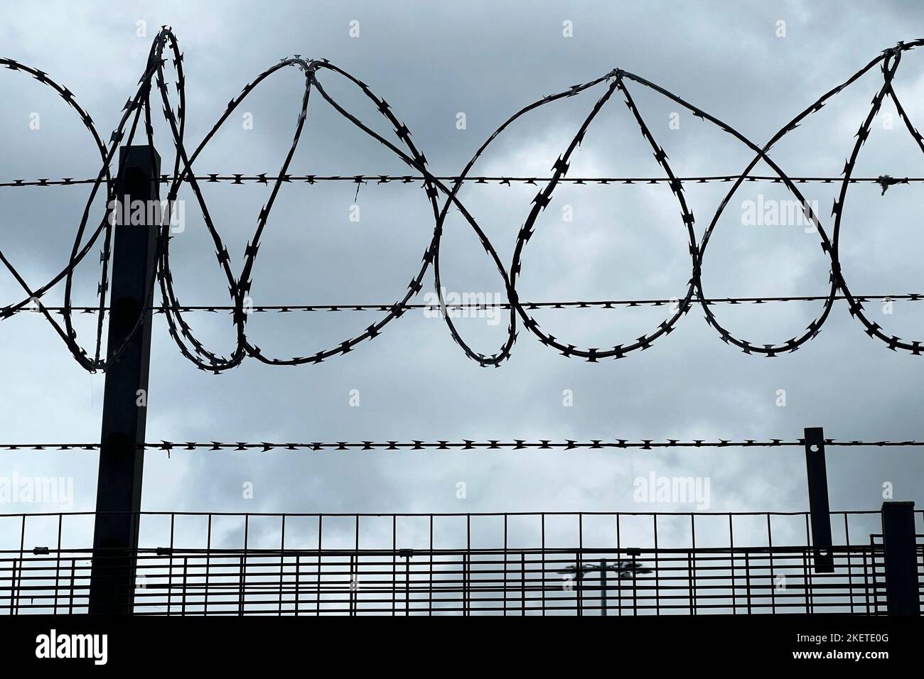 Security Concept With Razor Wire Fence And Camera Against Stormy Sky Stock Photo