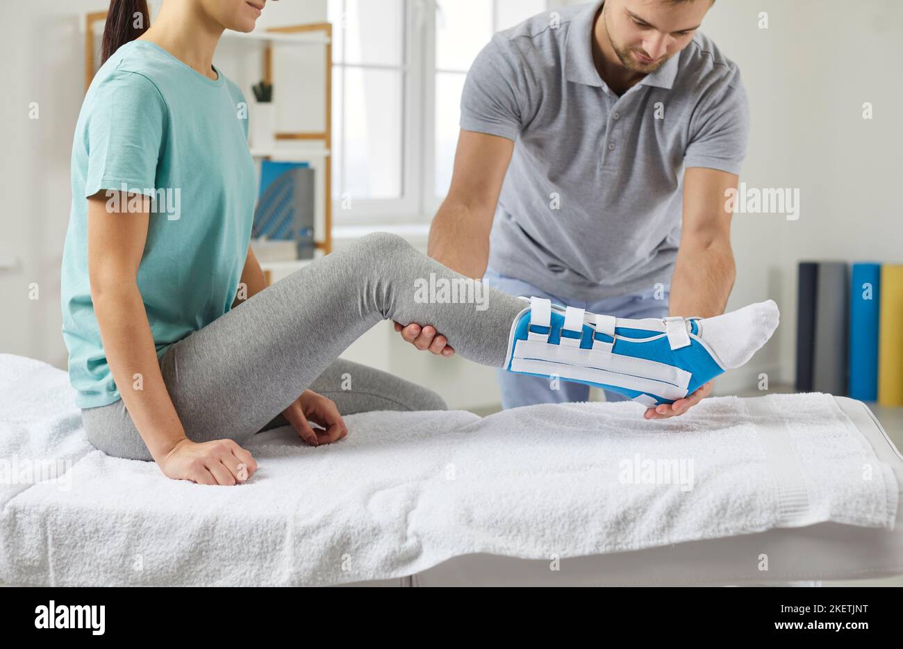 Male physiotherapist helps a woman put on a shin splint after leg surgery during rehabilitation medical consultation. Stock Photo
