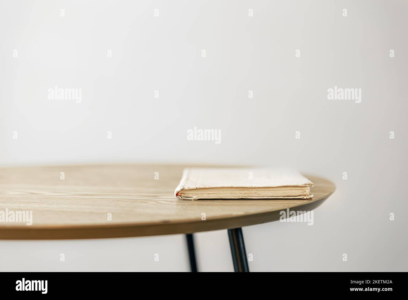 An old book on a small table against a white wall. Stock Photo