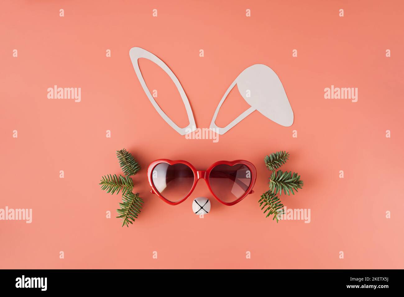 Minimalistic Christmas composition. Bunny face made from paper ears, heart shaped glasses, Christmas bell and spruce branches. Flat lay. 2023 year of Stock Photo