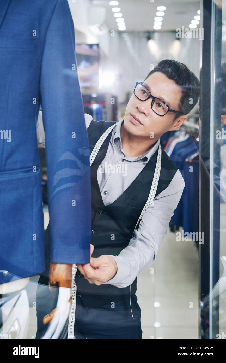 Vietnamese salesman putting mannequin with suit on in shop window Stock