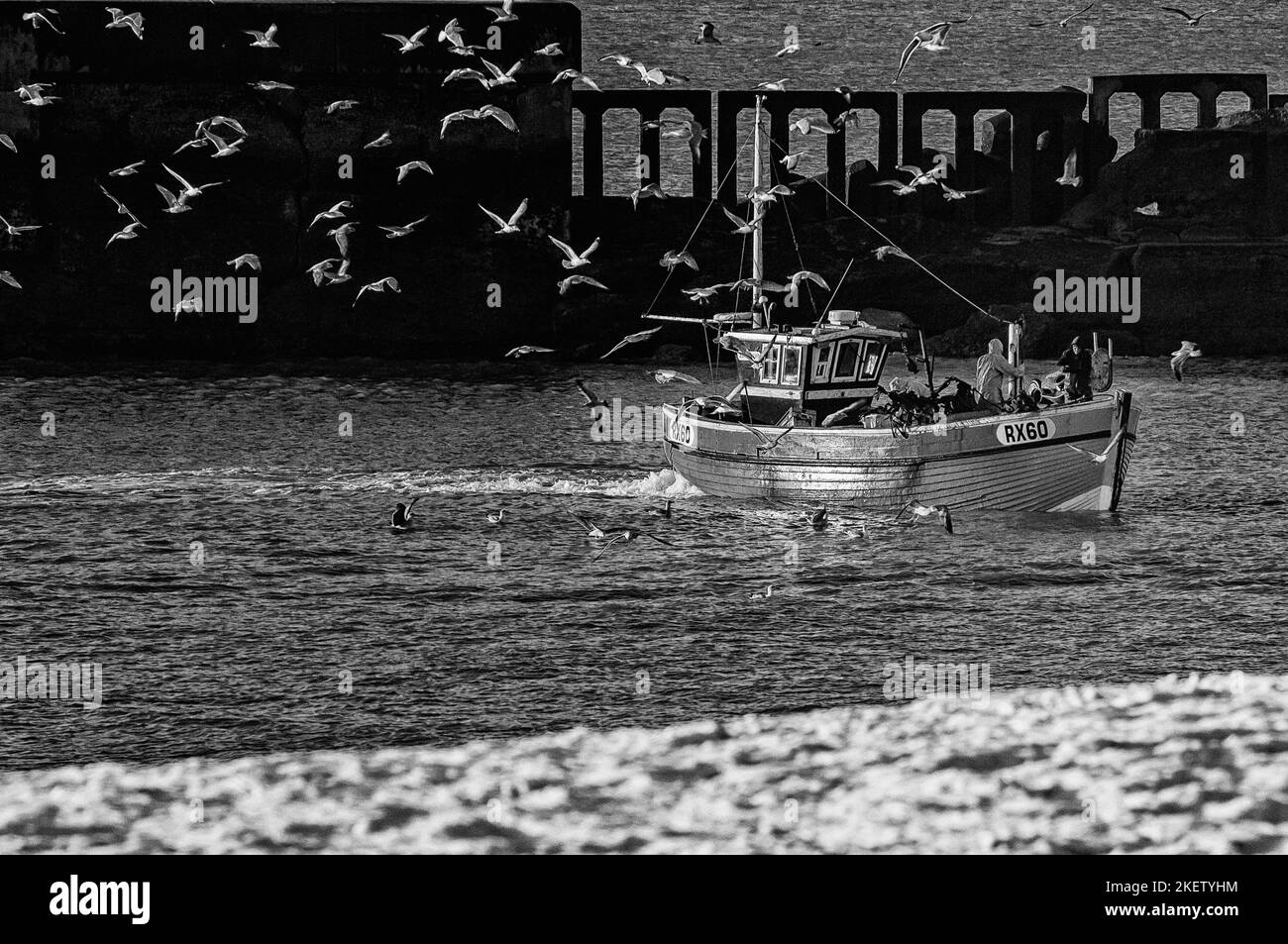 The Stade fishing beach, Old Town, Hastings. Fishermen bringing home their catch on a snow covered beach with a flock of herring gulls around them. East Sussex. England. UK Stock Photo
