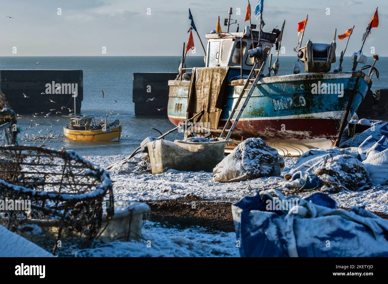 The Stade fishing beach, Old Town, Hastings. Fishermen bringing home their catch on a snow covered beach with a flock of herring gulls around them. East Sussex. England. UK Stock Photo