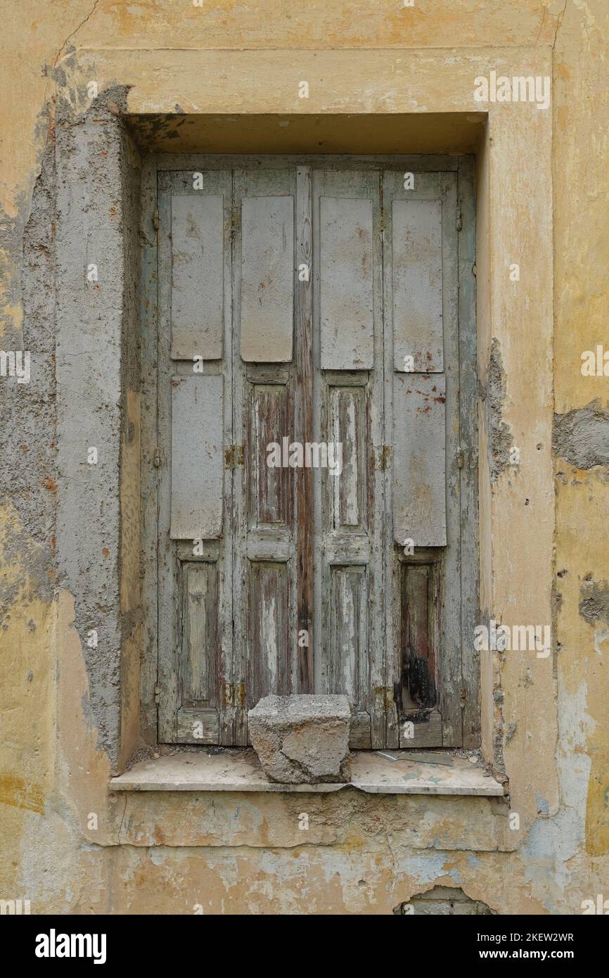 Old window with wooden shutter and weathered wall of an abandoned house. Stock Photo