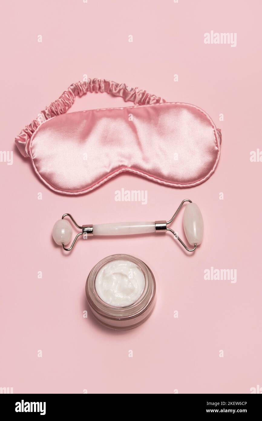 Face care concept. Pink silk sleeping mask, white jade facial roller