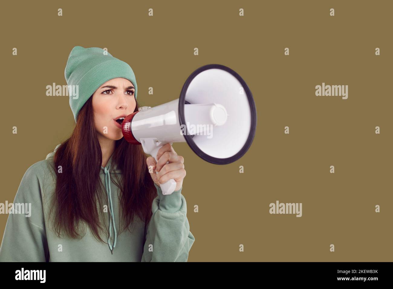 Serious female activist with megaphone in her hand makes loud announcement on brown background. Stock Photo