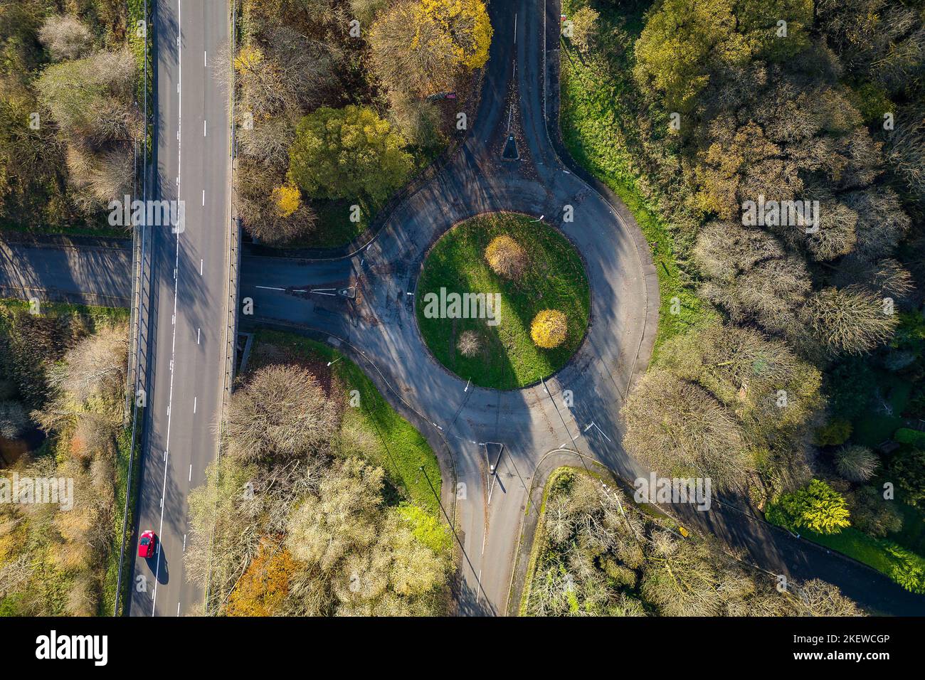 Traffic roundabout on a small road surrounded by trees displaying colorful fall leaves (Wales, UK) Stock Photo