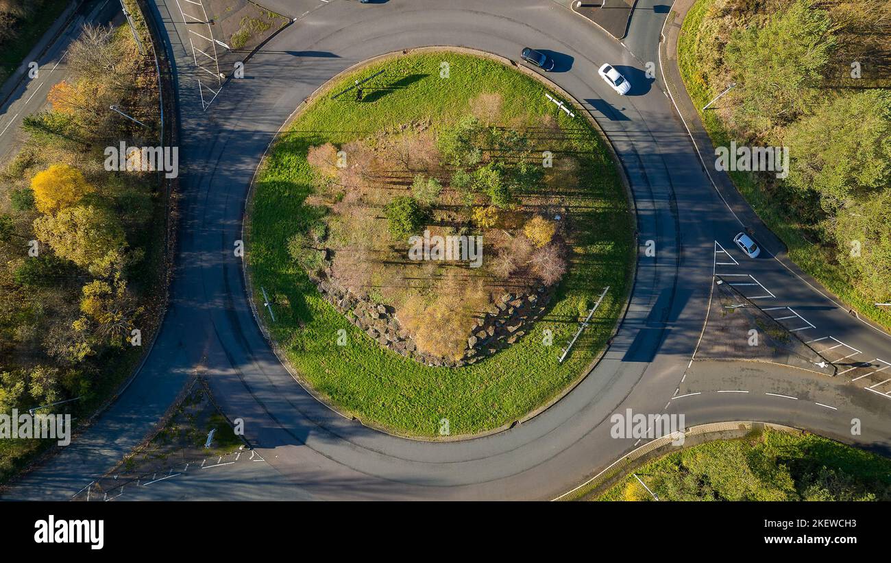 Traffic roundabout on a small road surrounded by trees displaying colorful fall leaves (Wales, UK) Stock Photo