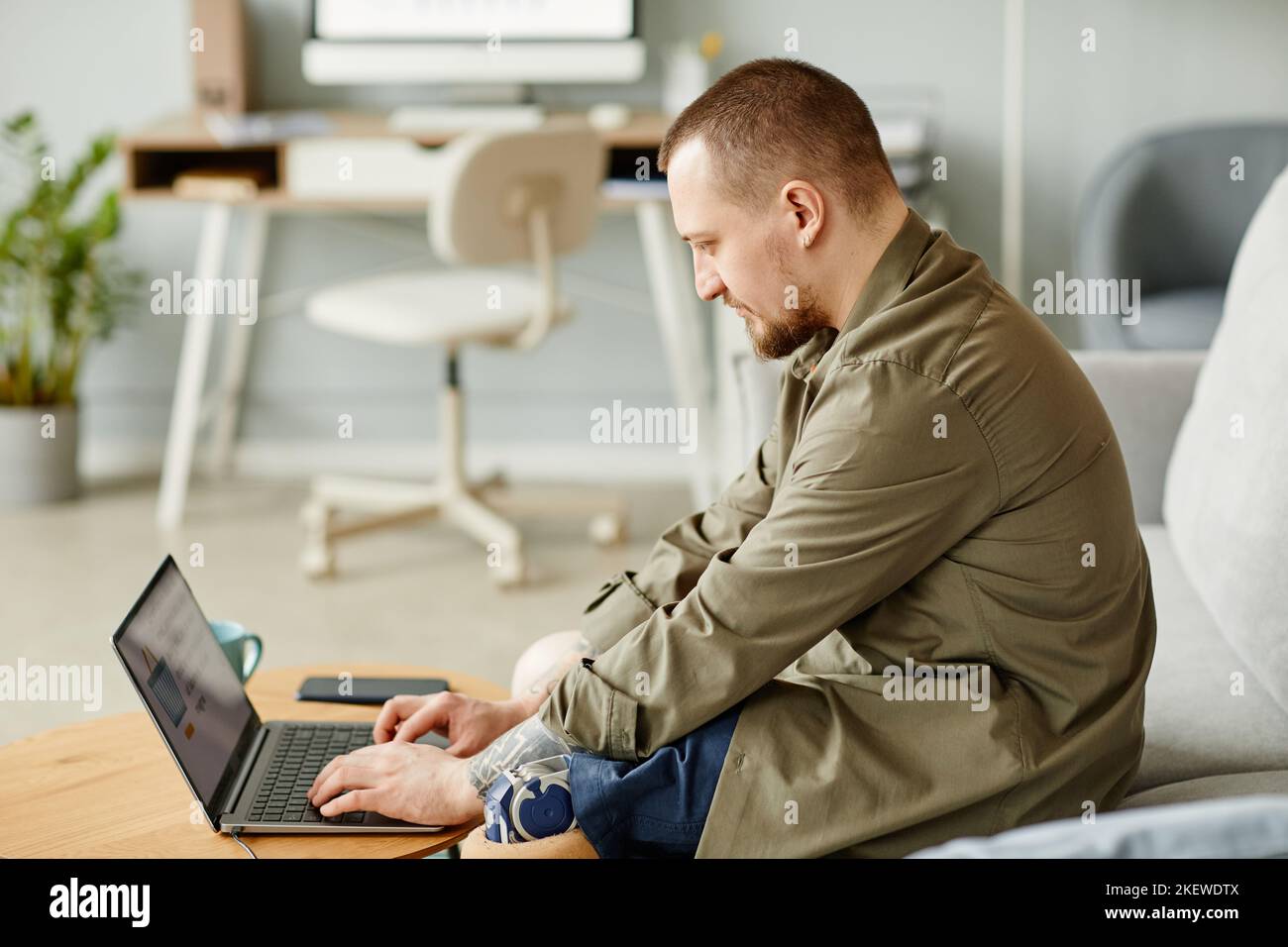 Side view portrait of man with prosthetic leg using laptop while working from home, copy space Stock Photo