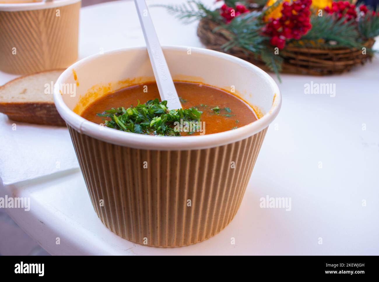 Goulash soup with spoon in paper bowl. Street food concept. Spicy meat soup. Street lifestyle. Travel cuisine. Tasty dinner. Delicious meal. Stock Photo