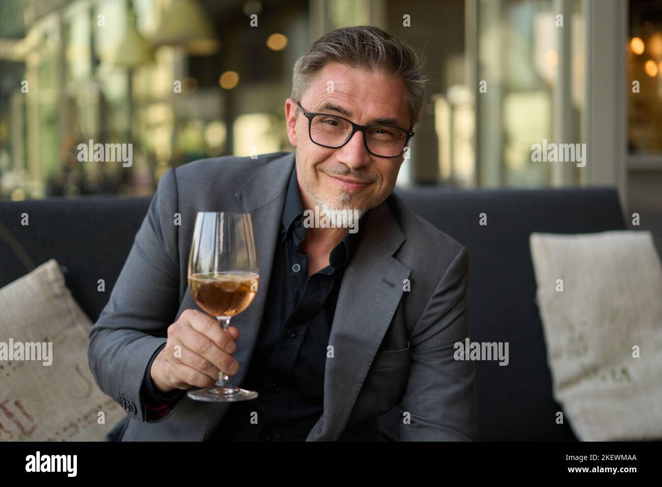 Older man sitting on coach drinking champagne based cocktail from wine