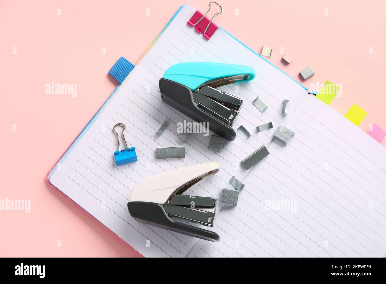 Open notebook, staplers and staples on pink background Stock Photo