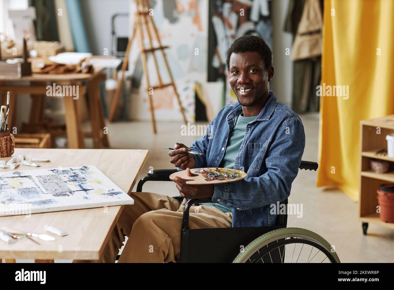 Young successful male artist with disability holding palette with mixed