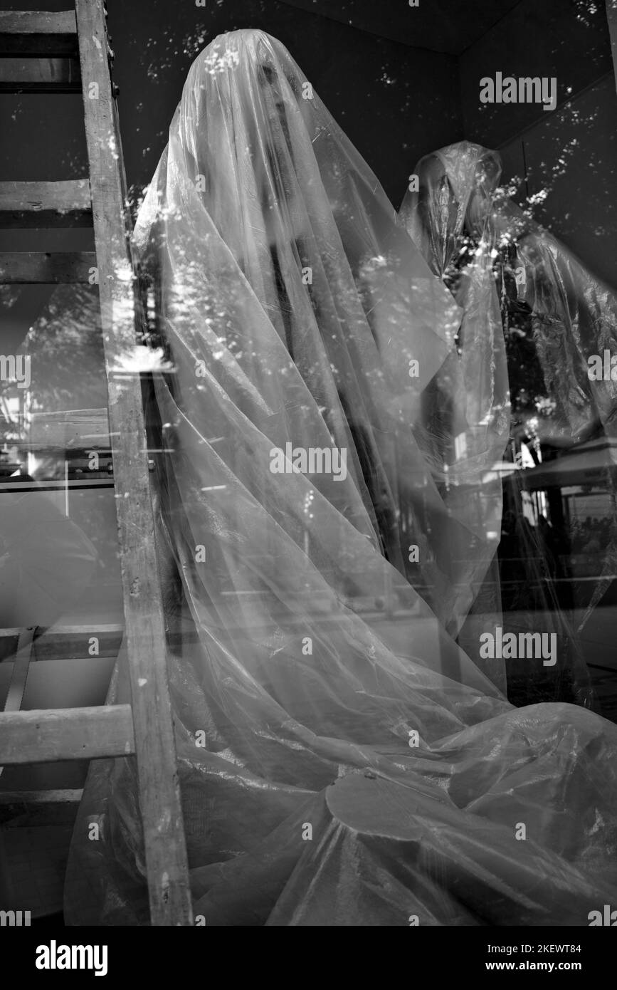 black and white shot of mannequins covered with plastic in a display ...