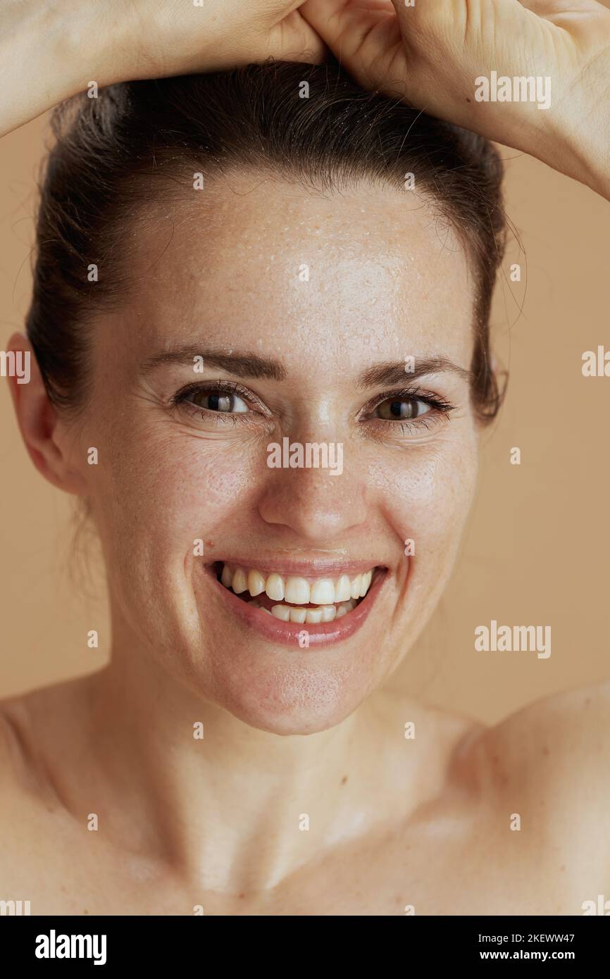 happy young woman with wet face washing against beige background. Stock Photo