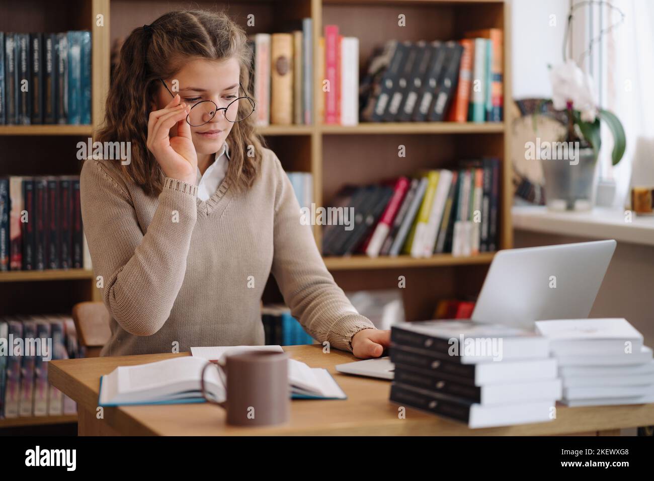 Attractive happy young girl student studying at the college library, sitting at the desk Stock Photo