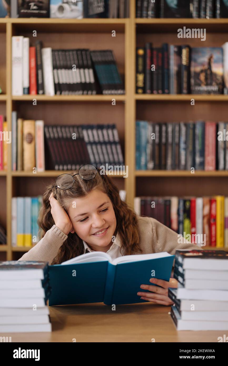 Attractive happy young girl student studying at the college library, sitting at the desk Stock Photo