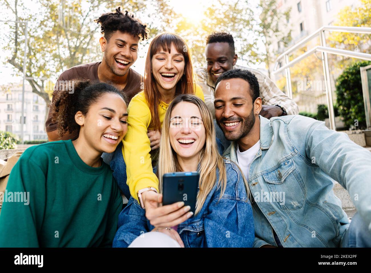 Young happy friends having fun together using mobile phone sitting outdoors Stock Photo