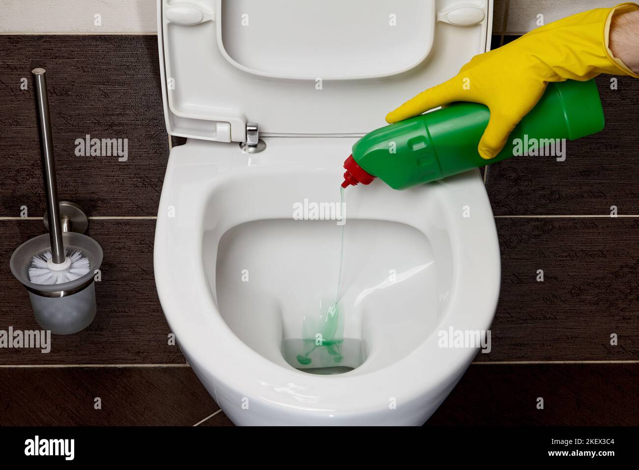 Toilet cleaning and disinfection. Hands in yellow rubber gloves pour