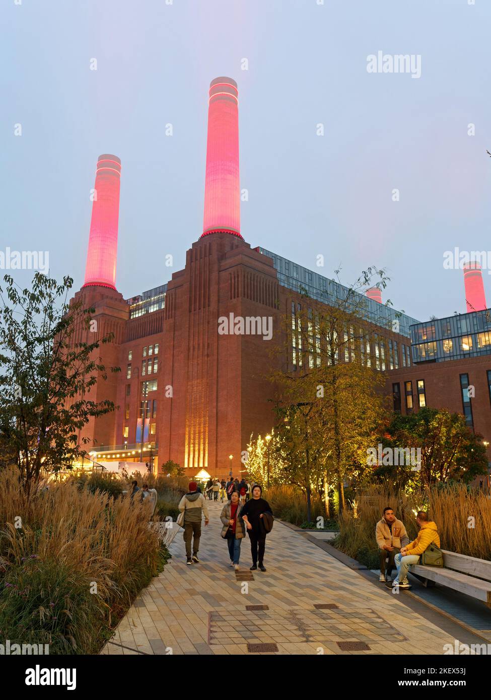 View looking up a path leading to Battersea Power Station in London illuminated at dusk with bright red chimneys piercing the sky Stock Photo
