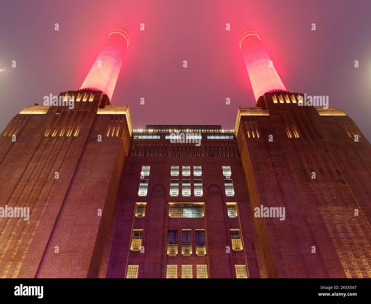 View looking up at Battersea Power Station in London illuminated on a misty night with bright red chimneys piercing the sky Stock Photo