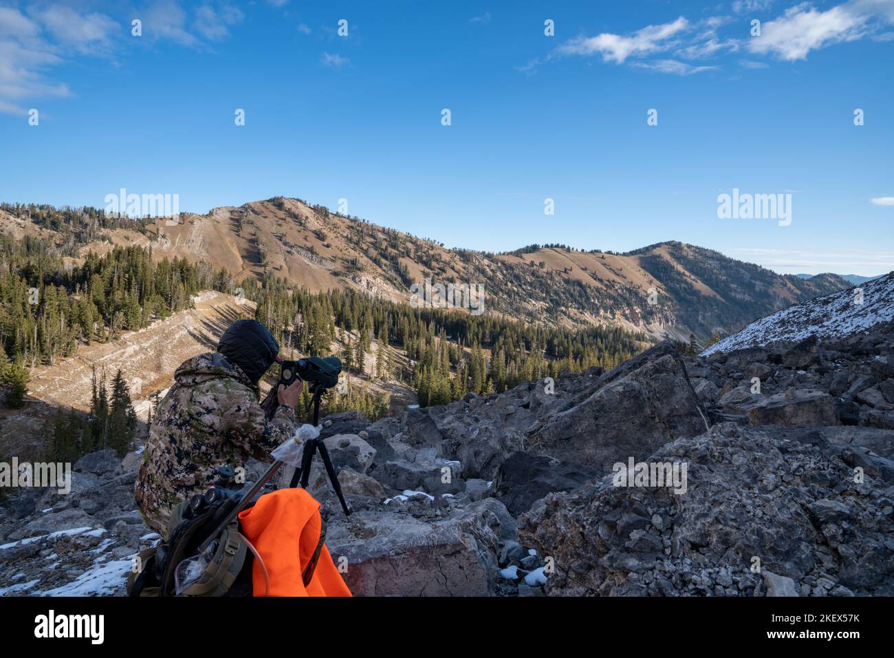 Hunter wearing camo uses his phone to take photos through a spotting scope while deer hunting in