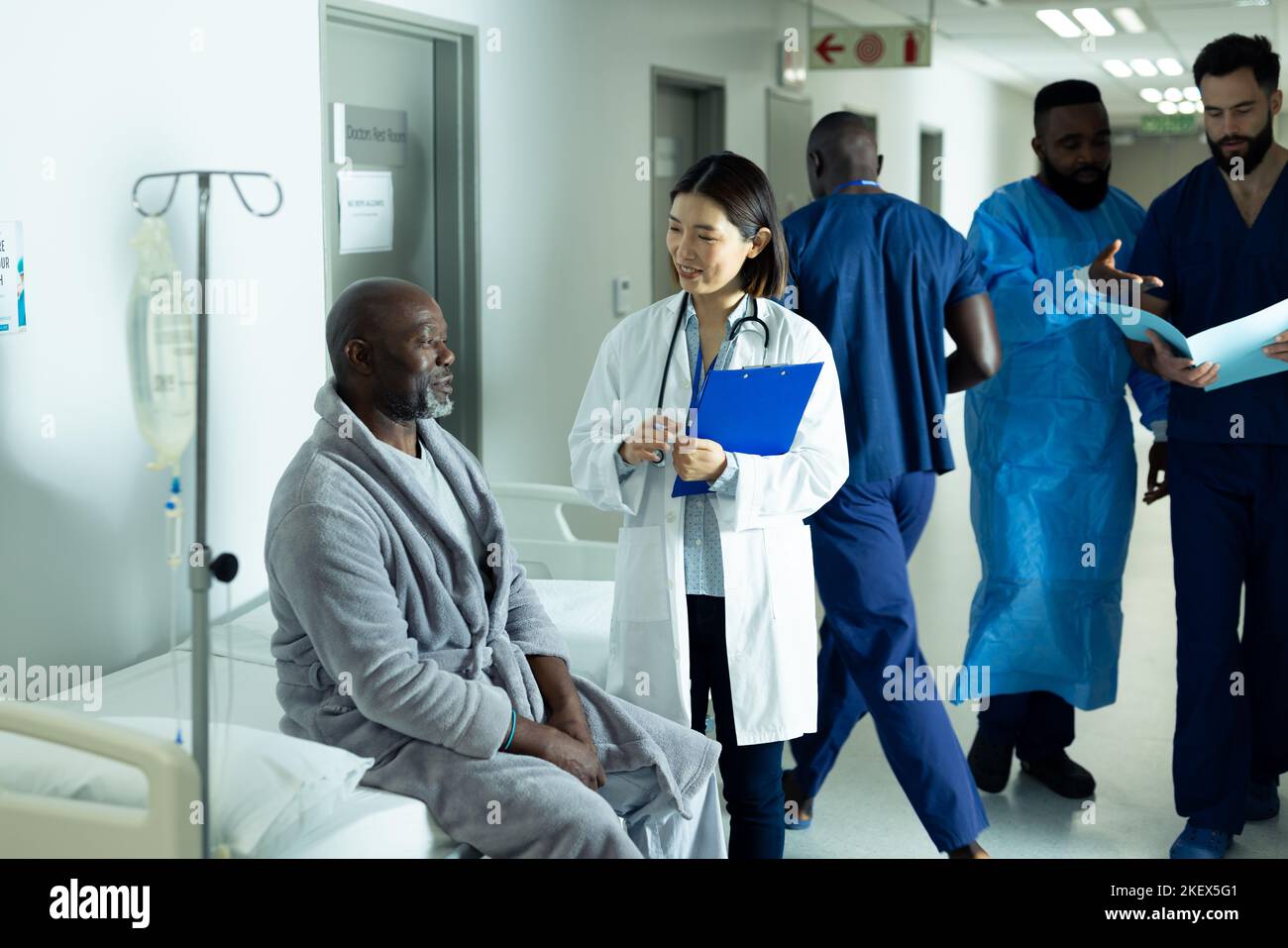 Happy asian female doctor and senior african american male patient talking in hospital corridor. Hospital, medical and healthcare services. Stock Photo