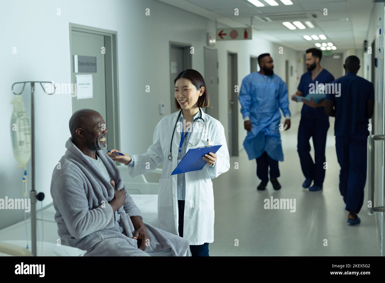 Asian female doctor and senior african american male patient smiling together in hospital corridor. Hospital, medical and healthcare services. Stock Photo