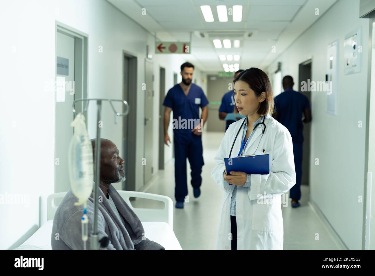 Asian female doctor and senior african american male patient talking in hospital corridor. Hospital, medical and healthcare services. Stock Photo