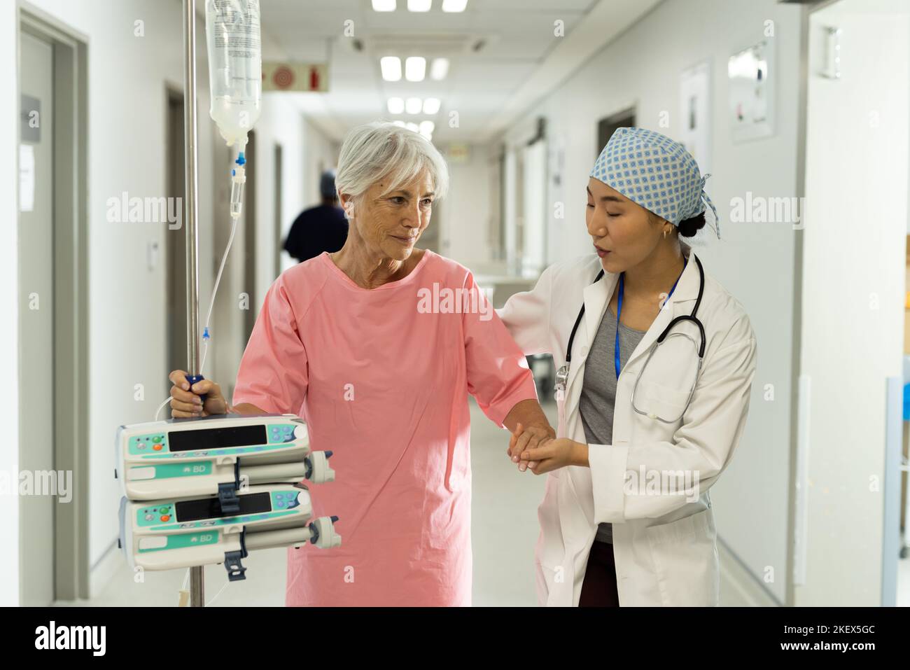 Diverse female doctor and caucasian senior female patient with iv pole talking. Hospital, medical and healthcare services. Stock Photo