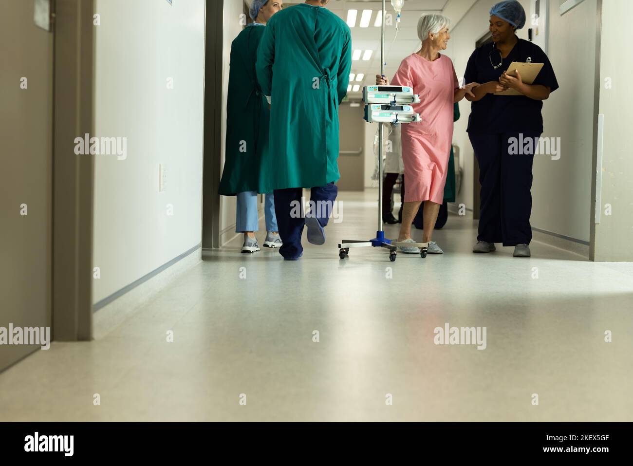 Diverse female doctor and caucasian senior female patient with iv pole talking in hospital. Hospital, medical and healthcare services, copy space. Stock Photo