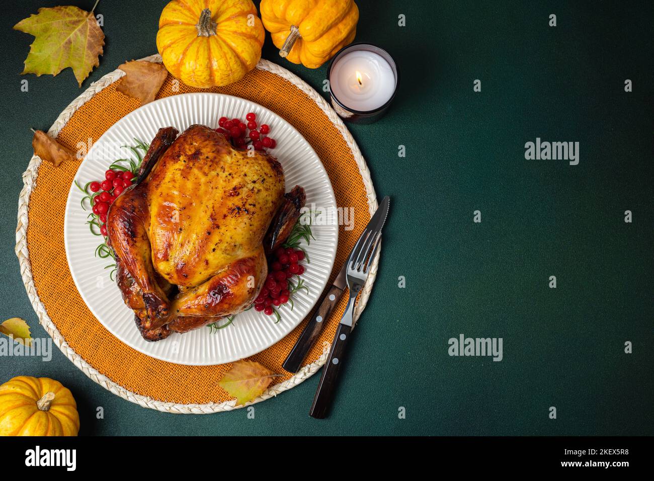 Roasted whole chicken or turkey with autumn vegetables for thanksgiving dinner on green background. Happy Thanksgiving background. Copy space Stock Photo