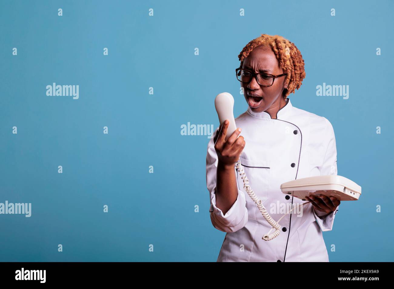 Annoying eatery woman chef yelling on landline call. Angry kitchen manager arguing on phone. African american female restaurant worker fighting loudly on audio call. Stock Photo