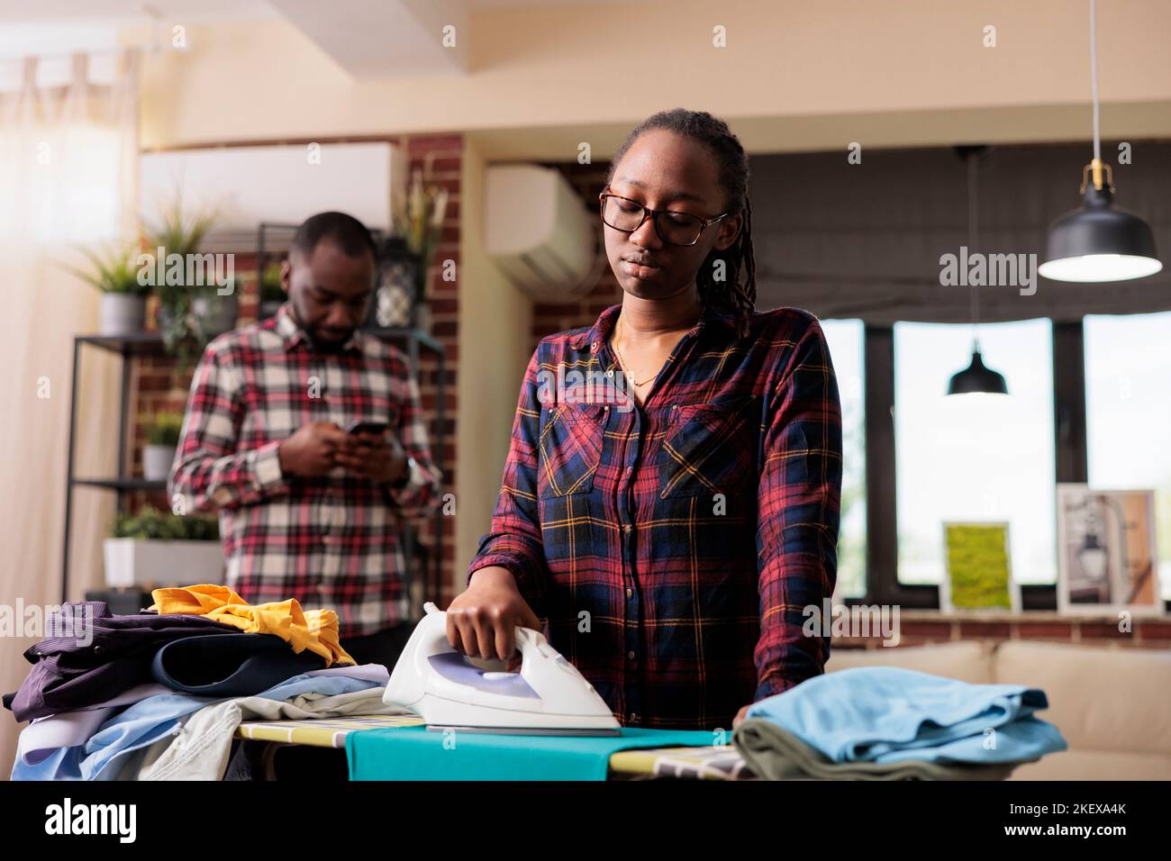 Depressed african american housewife ironing laundry husband uses cell phone without paying 